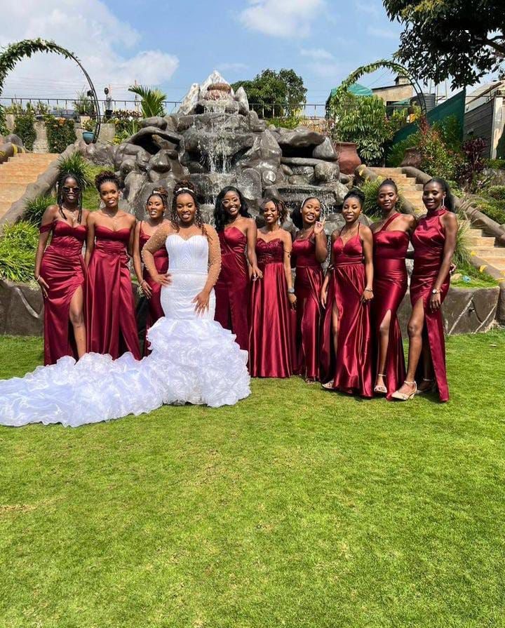 She's Confident bridal party, bride in an ivory mermaid gown with eight bridesmaids in deep red satin at a garden venue with stone fountain