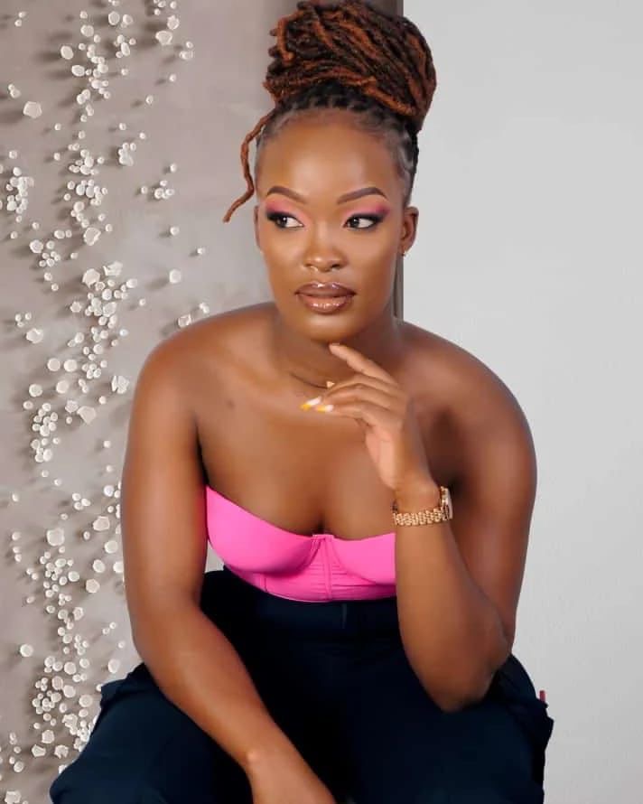 Studio portrait, long burgundy locs in a high updo, soft pink eye look and glossy nude lip, pink strapless top against a textured neutral backdrop