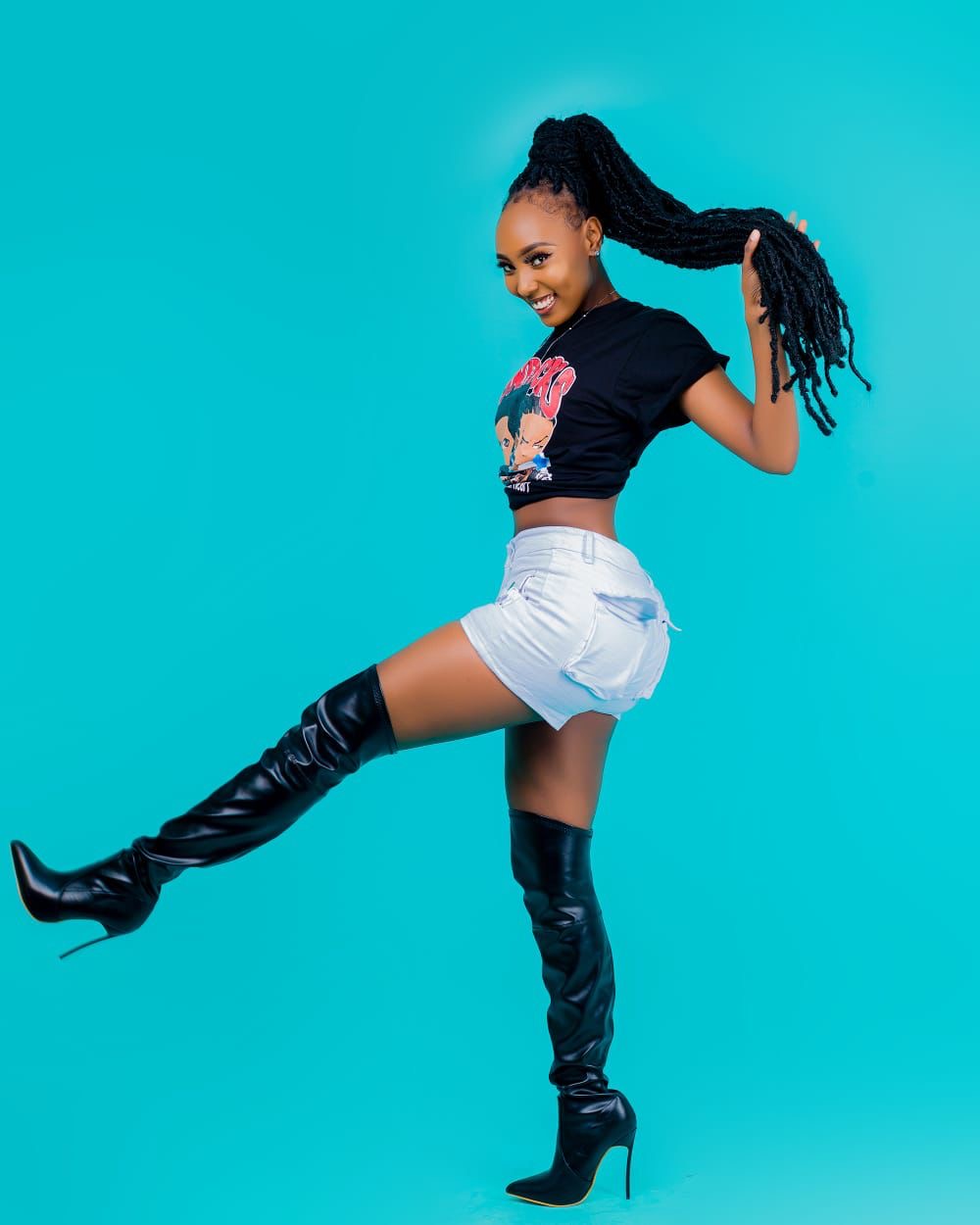 Studio action shot, long braided ponytail mid-swing, graphic black tee with white shorts and tall black boots, teal seamless backdrop