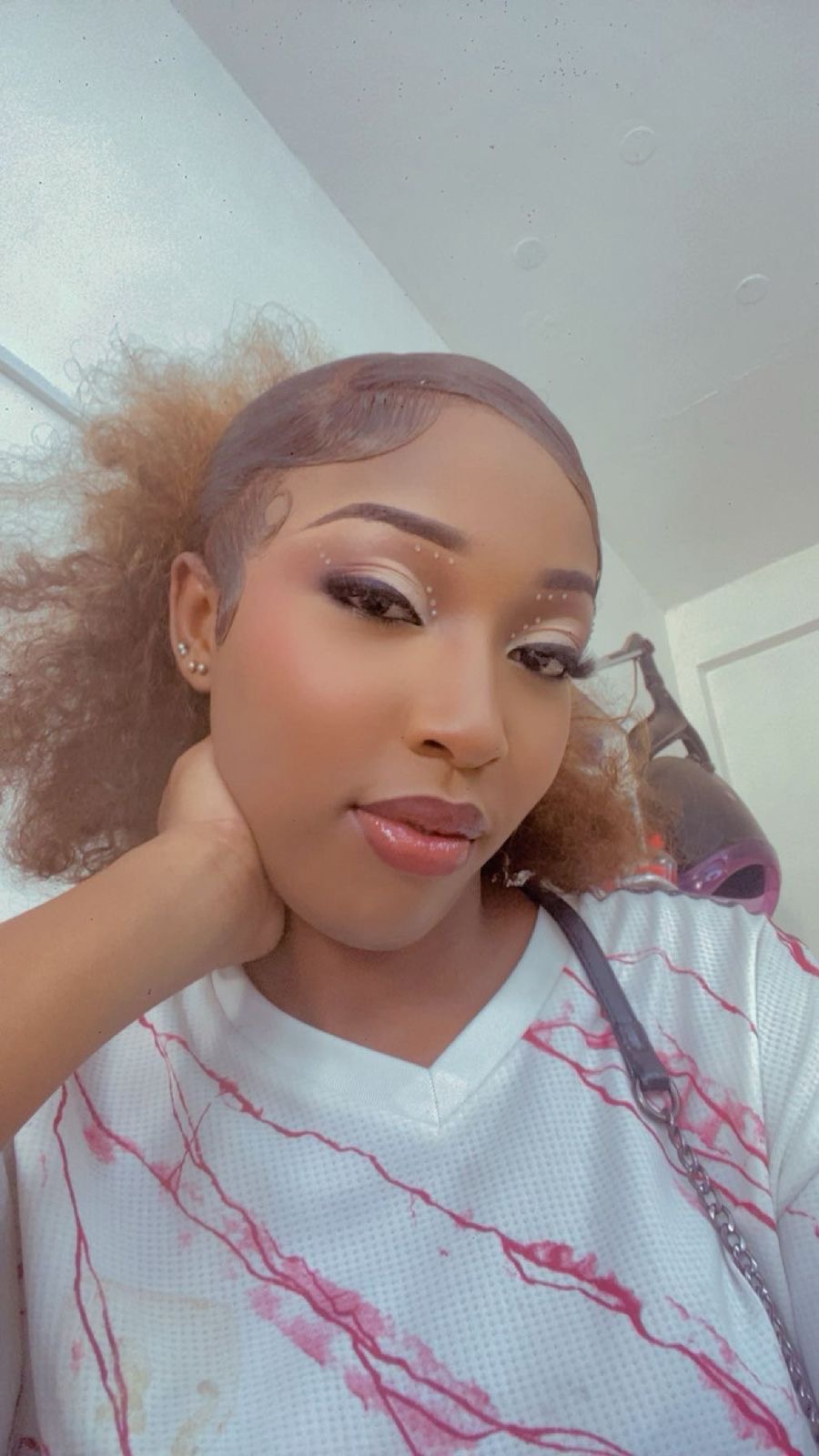 Beauty selfie, sleek auburn hair, graphic black liner with crystal accents and glossy nude lip, close portrait in a salon